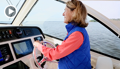 A smiling woman captaining a Grady-White boat with an iPad running the Captain Grady app on the helm